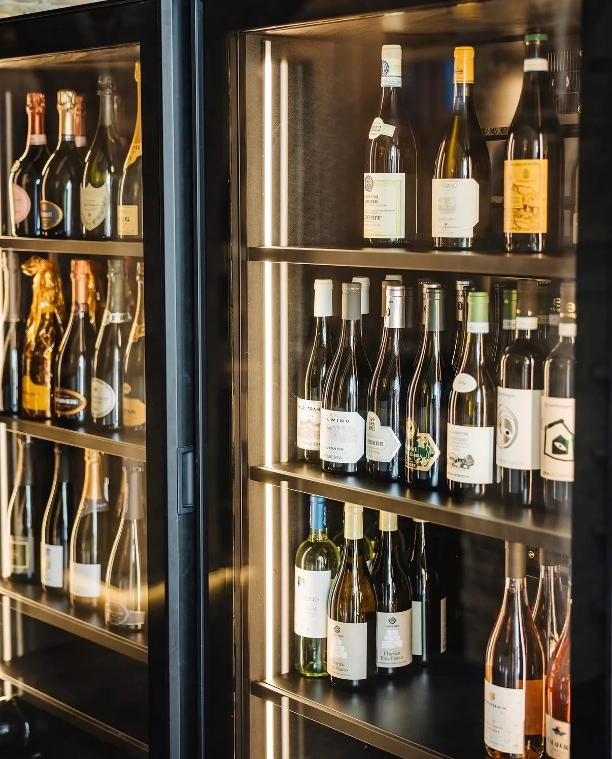 Vetrina-cantina di Macallè con bottiglie di champagne e vini bianchi illuminate