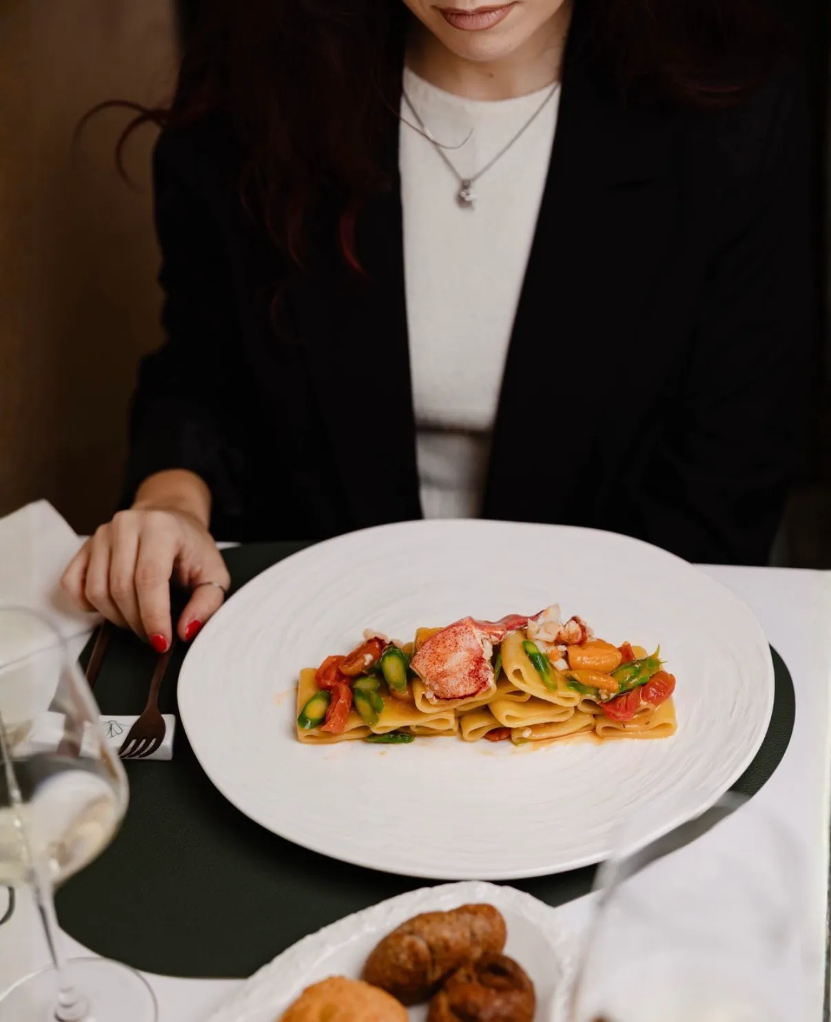 Paccheri con astice, asparagi e pomodorini serviti in un piatto bianco