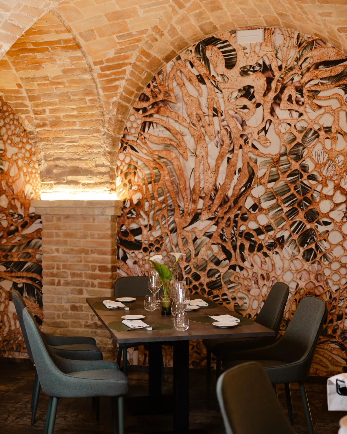 Tavolo apparecchiato sotto l’arco in mattoni, davanti alla parete decorata a bassorilievo con motivi di corallo